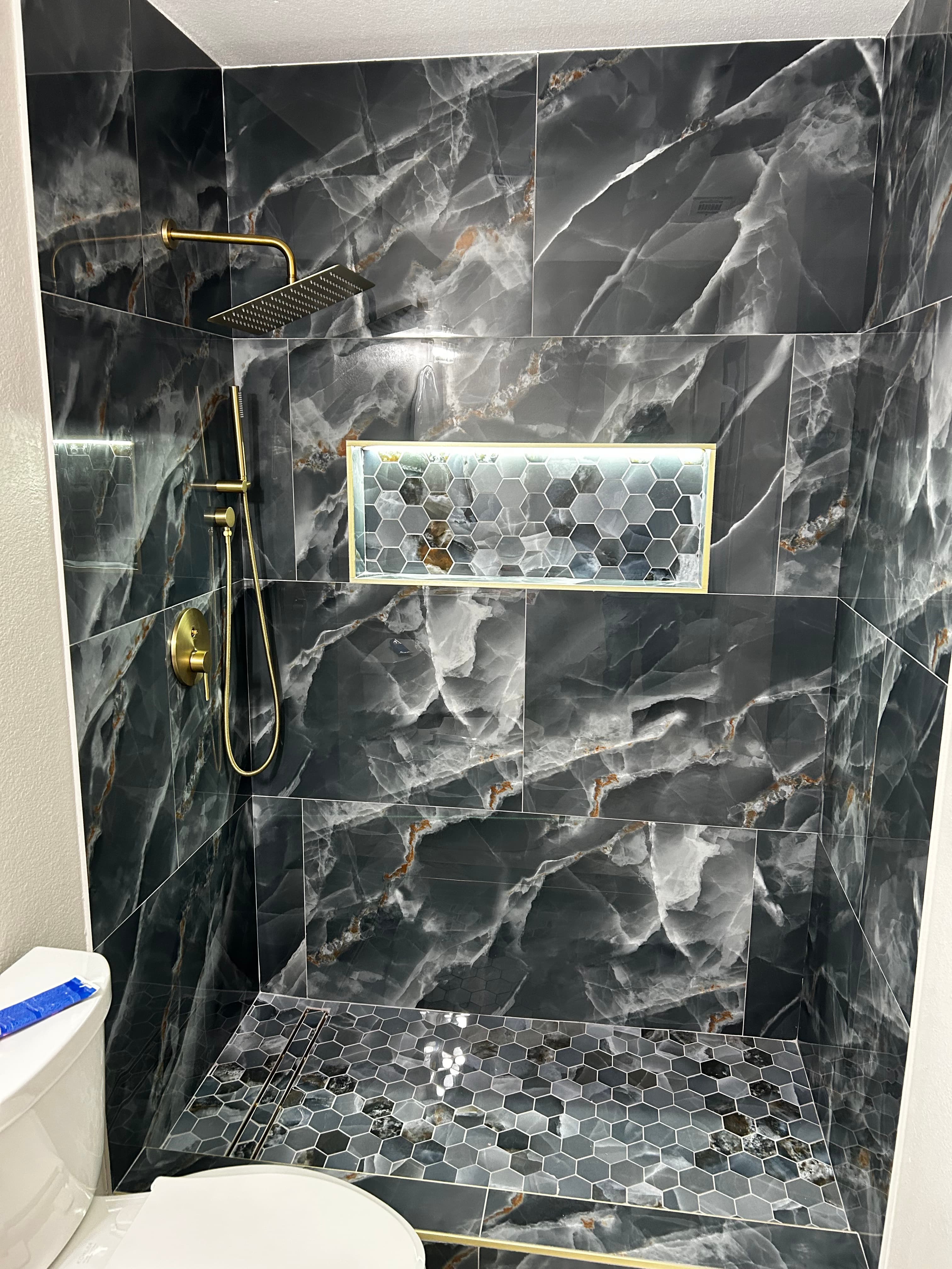 Luxury bathroom remodel by HN Construction with dark onyx-look marble tile, a lit hexagon shower niche, and brushed-gold fixtures