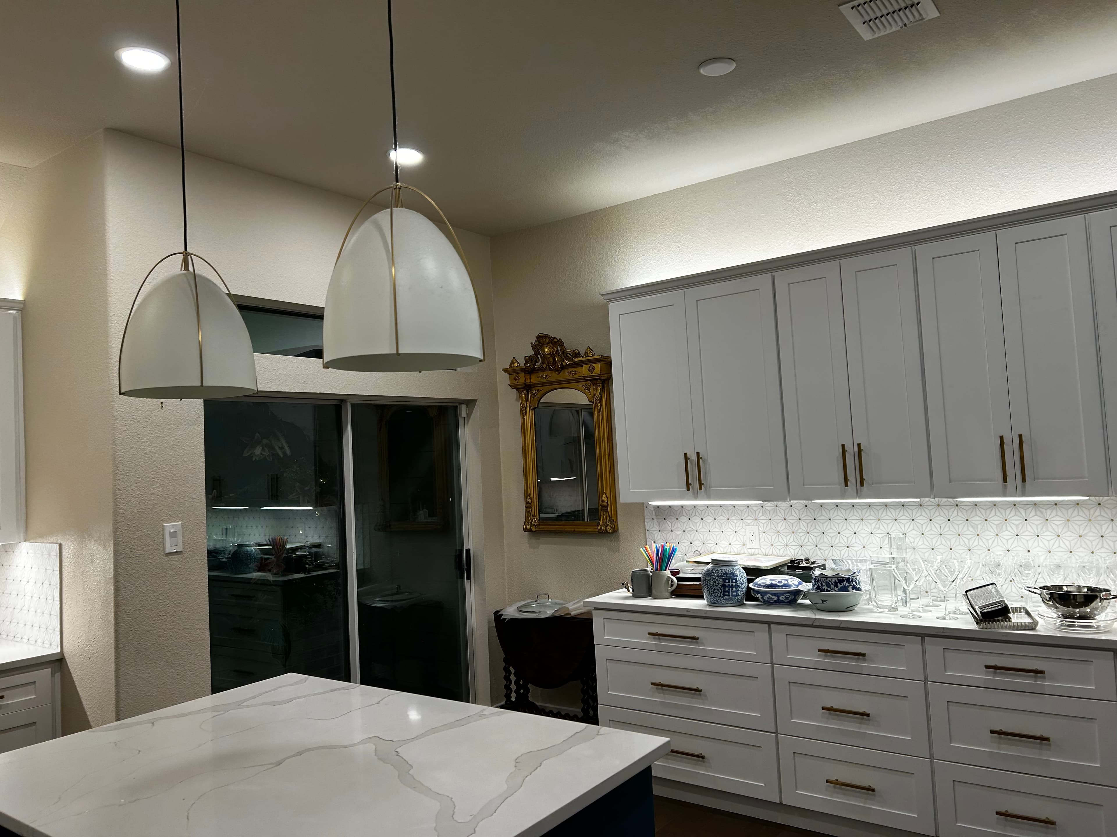 Modern white kitchen remodel by HN Construction with white shaker cabinets, brass hardware, a geometric white tile backsplash, and under-cabinet lighting