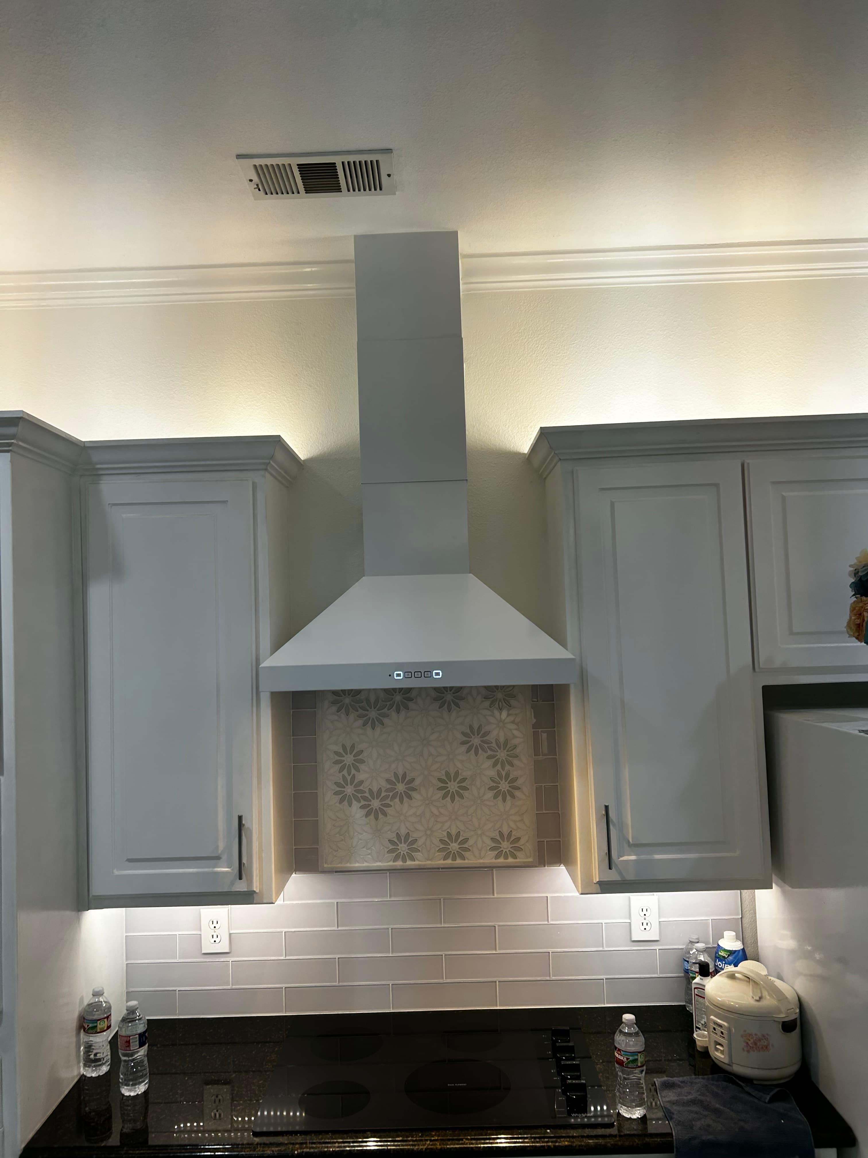Custom white range hood over a cooktop with a daisy-pattern tile backsplash in a white kitchen