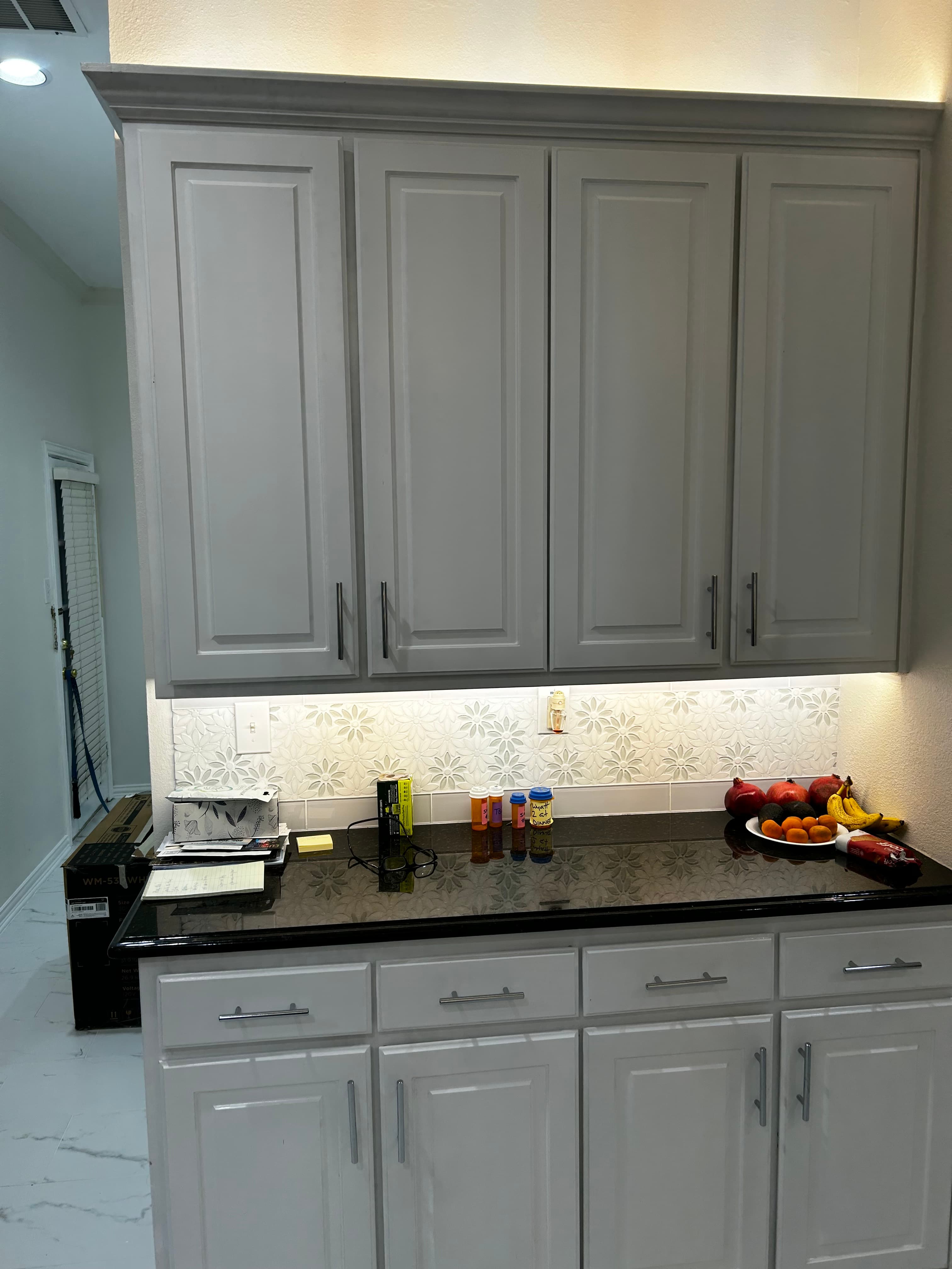 Floor-to-ceiling white kitchen cabinetry with brushed hardware and a floral tile backsplash