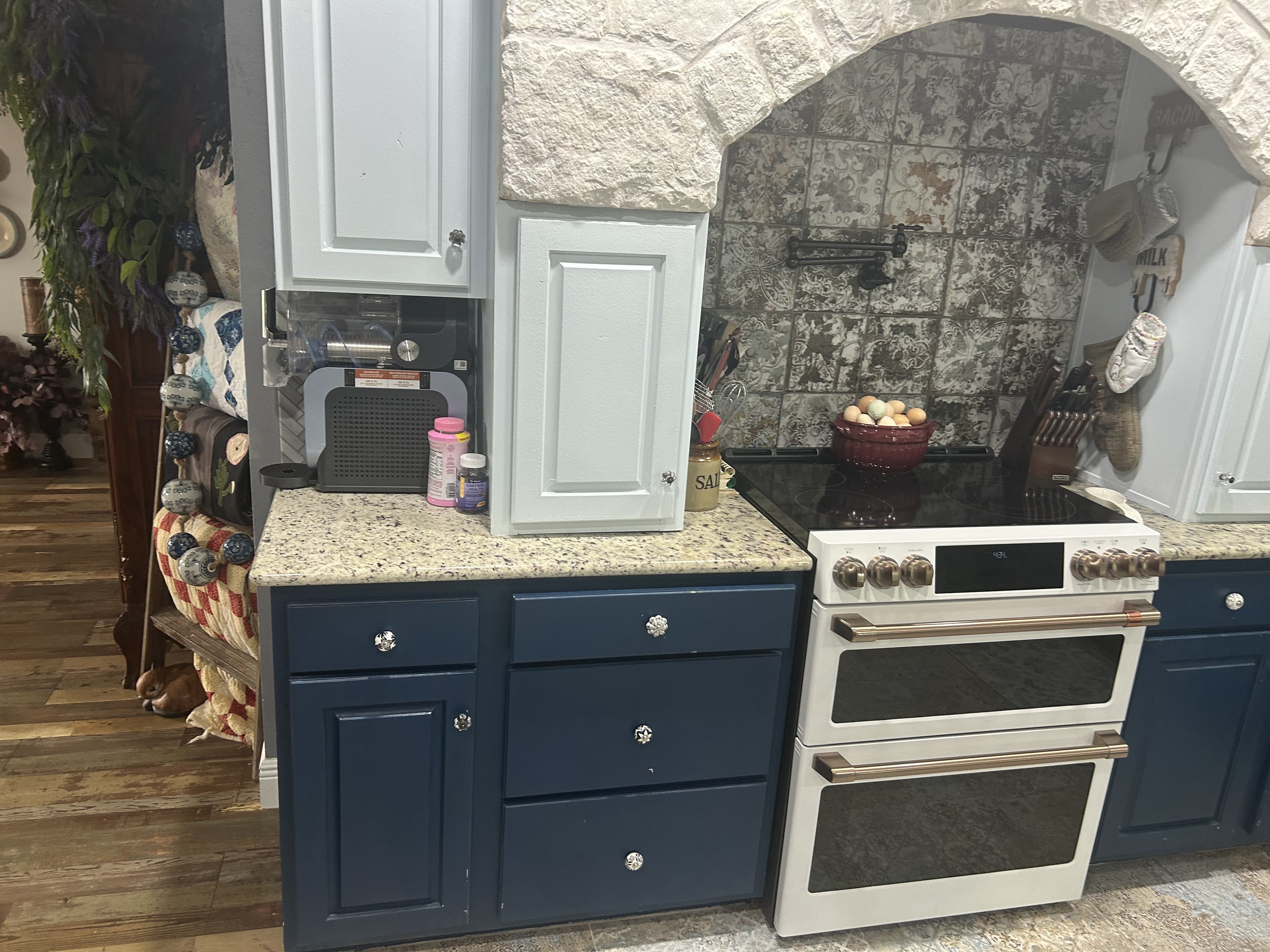 Navy and white farmhouse kitchen with granite counters, herringbone tile, and matte-white appliances with brushed-bronze handles