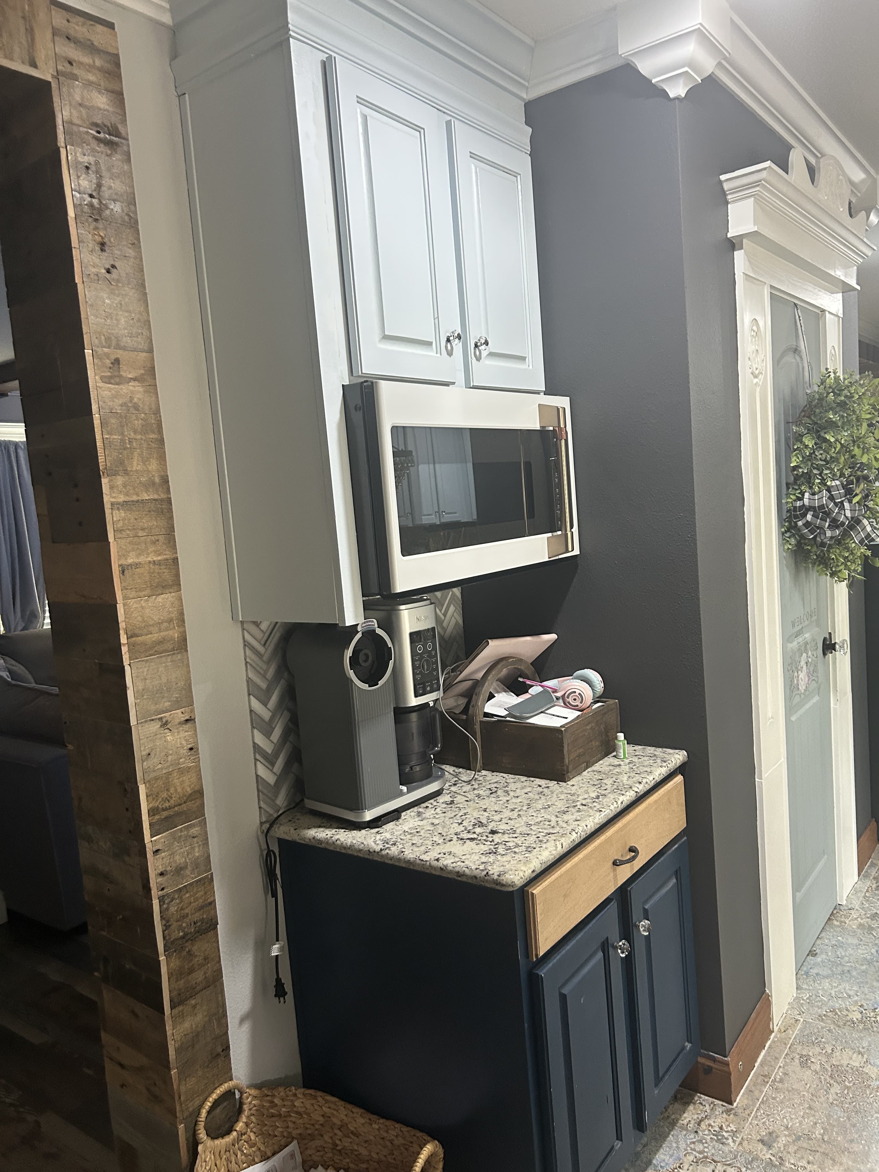 Farmhouse kitchen nook with white upper cabinets, a navy base cabinet, granite counter, and a reclaimed-wood accent column