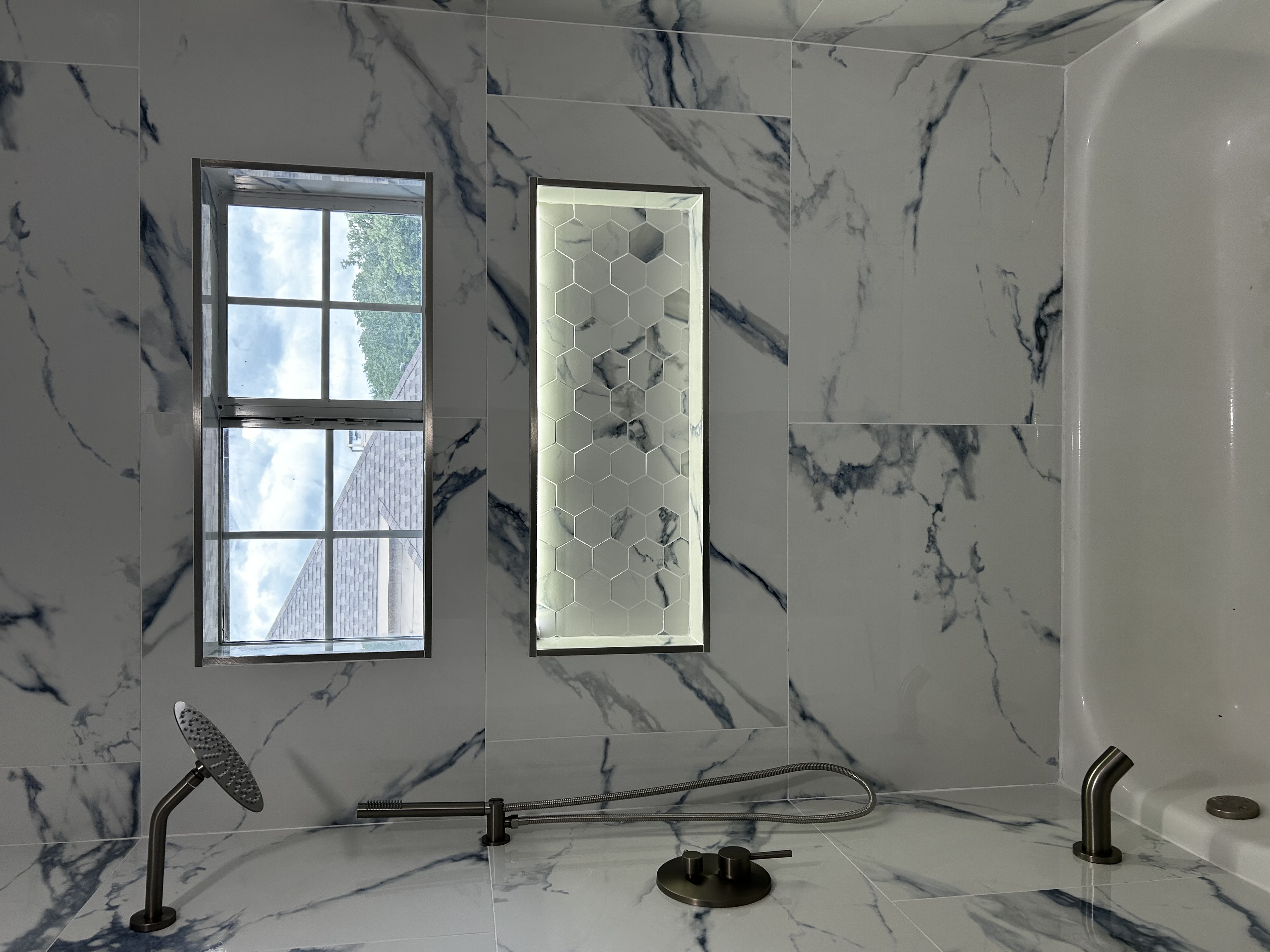 Bright bathroom remodel with white-and-blue marble-look tile, a lit hexagon shower niche, and a soaking tub