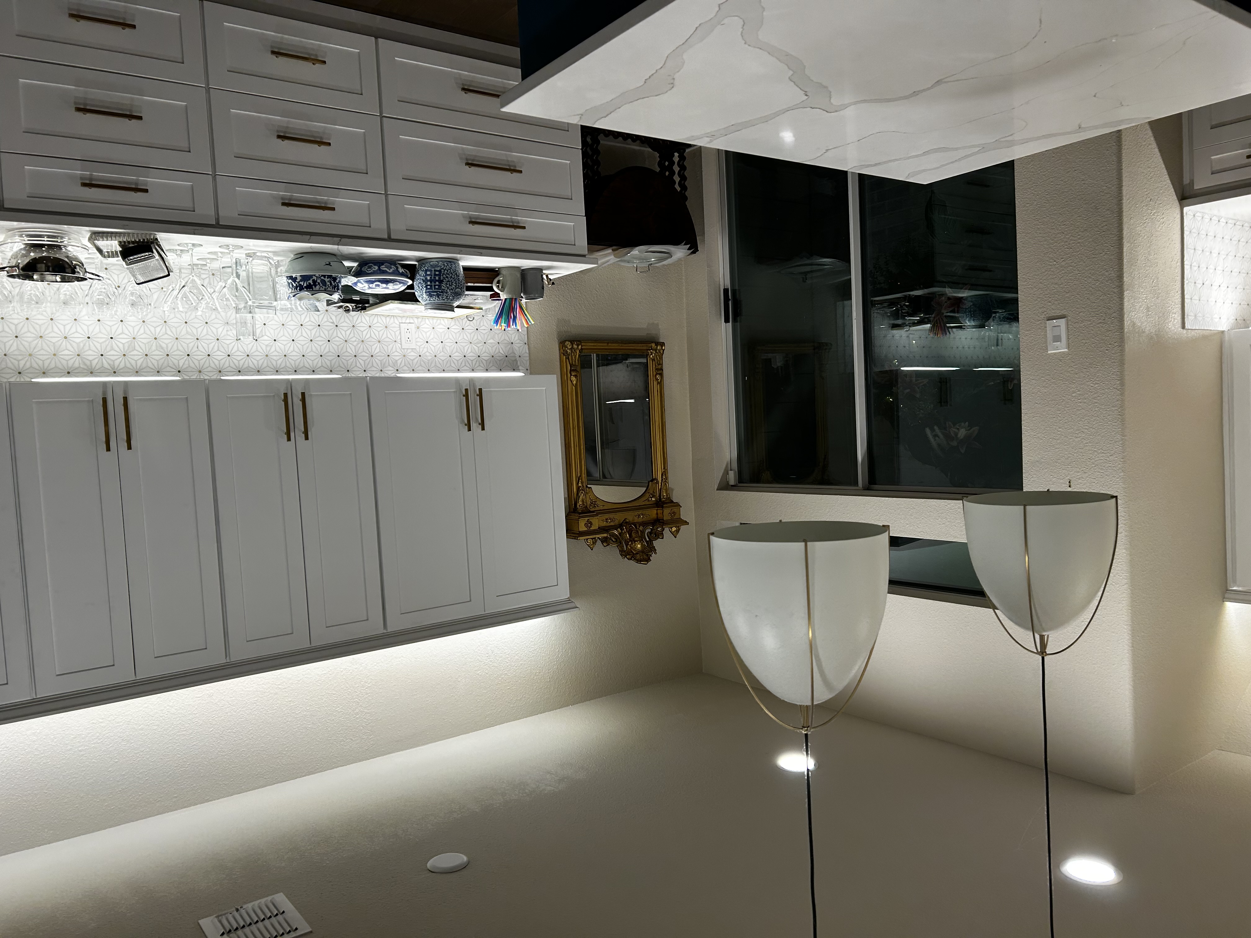 Modern white kitchen remodel by HN Construction with white shaker cabinets, brass hardware, a geometric white tile backsplash, and under-cabinet lighting
